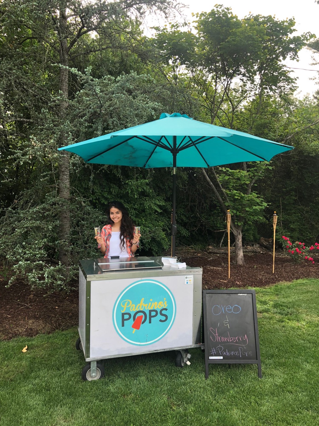 The Padrino's Pops cart under a teal umbrella at an outdoor event